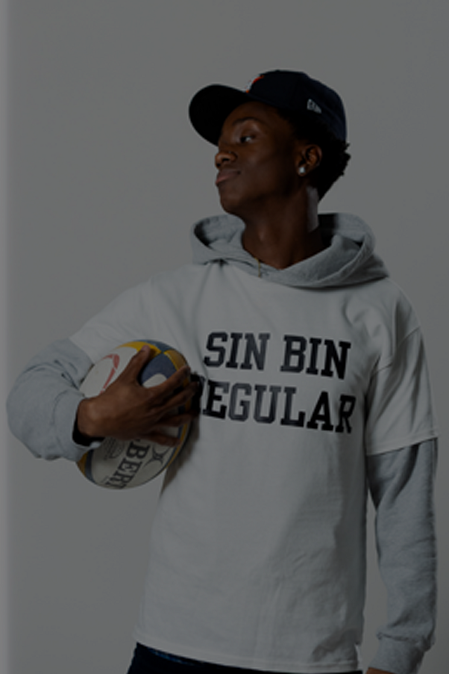 Person wearing a hoodie with 'SIN BIN REGULAR' text, holding a sports ball against a plain background